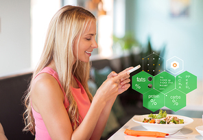 eating, technology and people concept - happy woman with smartphone and salad for lunch at restaurant over food nutritional value chart