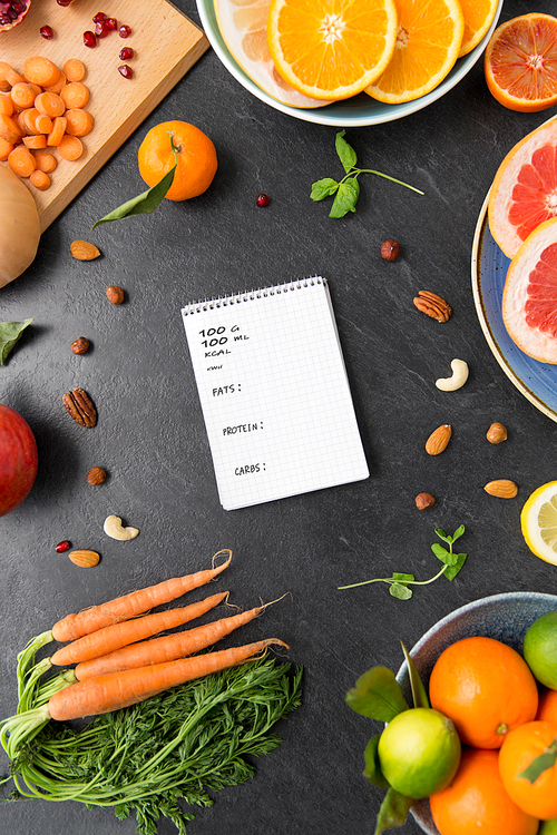 healthy eating, food and diet concept - close up of notebook, fruits and vegetables on slate table top with nutritional value