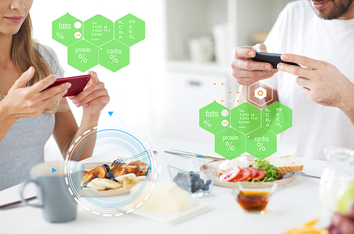 eating, people and technology concept - close up of couple with smartphones having breakfast at home over food nutritional value chart