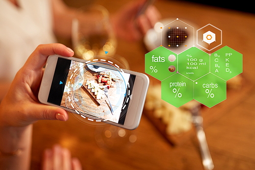 technology, eating and people concept - hands with food on smartphone screen at restaurant over nutritional value chart