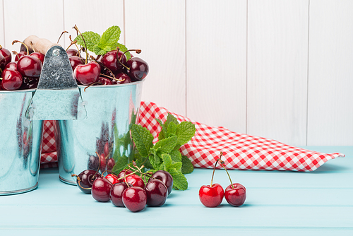Cherries in two small metal buckets on the wooden table.