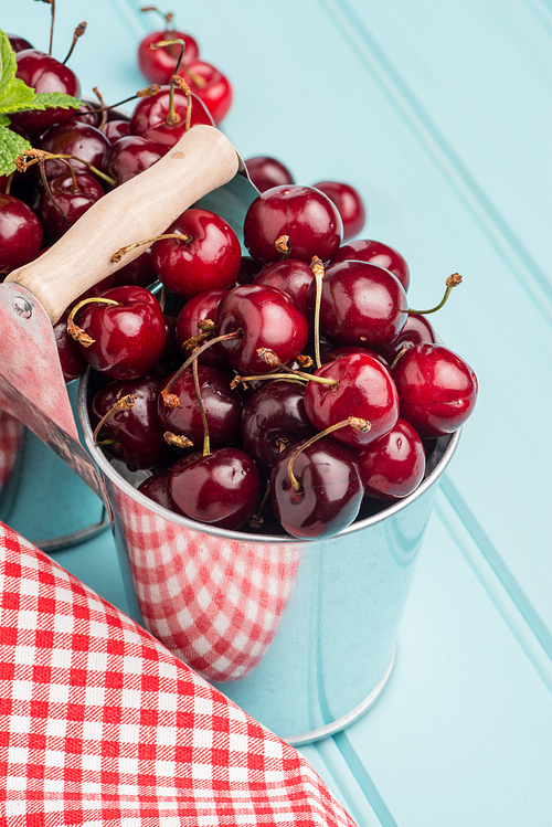 Cherries in two small metal buckets on the wooden table.