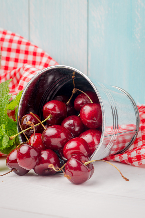 Cherries in small metal bucket on the wooden table.