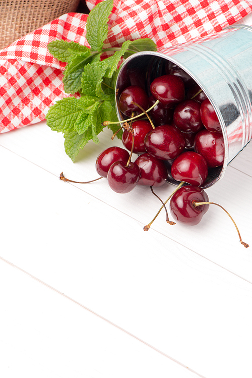 Cherries in small metal bucket on the wooden table.