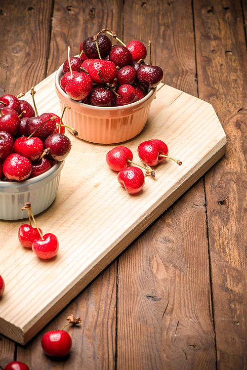 Red ripe cherries in ceramic bowls on wooden kitchen countertop.
