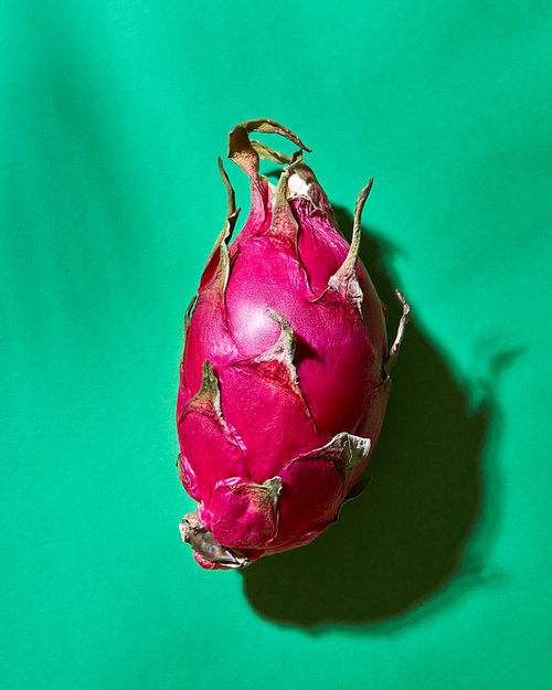 A whole exotic fruit pitahaya with a reflection of shadows on a green background. Top view