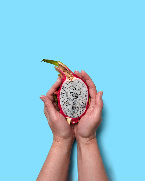 The girl's hands hold half of the juicy fresh fruit pitahaya on a blue background with a space for the text. Flat lay