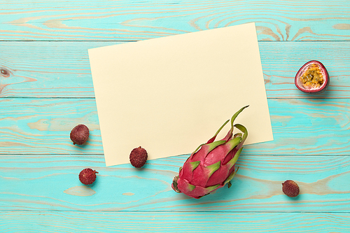 White cardboard with passion fruit, pitahaya and lychee on a blue wooden background with space for text. Card. Flat lay