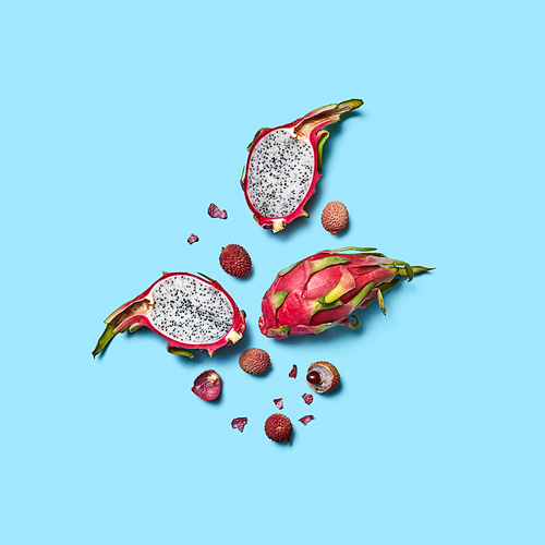 Appetizing whole and halves of lychee and pitahaya fruit on a blue background with space for text. Exotic healthy fruits. Flat lay