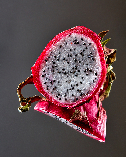 Half of the ripe pitahaya or Dragon fruit is reflected on a black glossy background