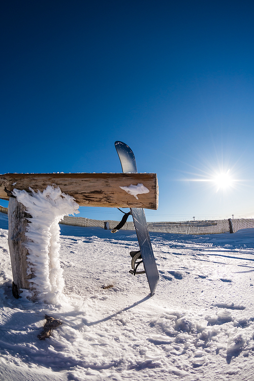 Snowboard leaning on a wood rail on a winter snow covered mountainside and sun shine in blue sky.