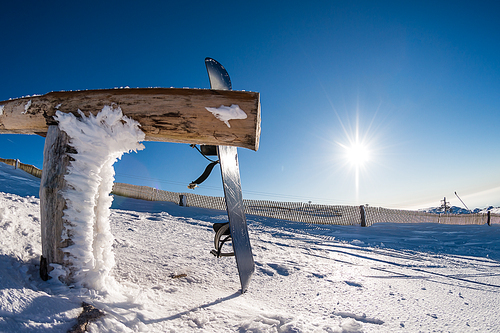 Snowboard leaning on a wood rail on a winter snow covered mountainside and sun shine in blue sky.