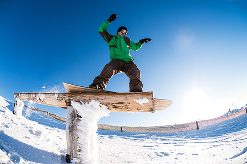 A snowboarder executes a radical slide on a rail in a snow park.
