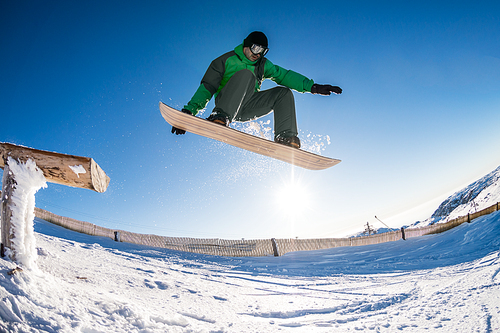 Snowboarder jumping from a wood rail against blue sky.