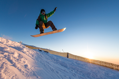 Snowboarder at jump in mountains at sunset sky.