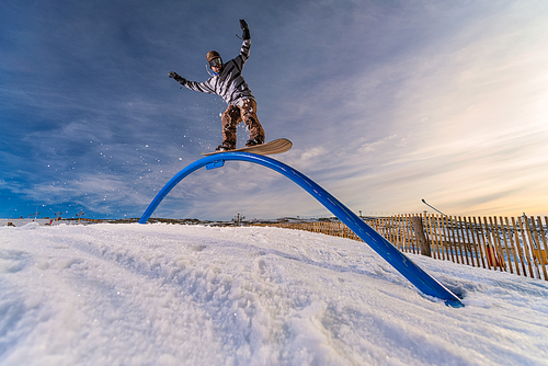 A snowboarder executes a radical slide on a rail in a snow park.
