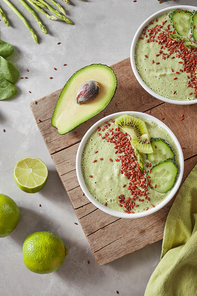 Vegetarian food smoothies from green organic vegetables with flax seeds and lime slices in a white bowl on a wooden board, served with a textile green towel on a grey background.