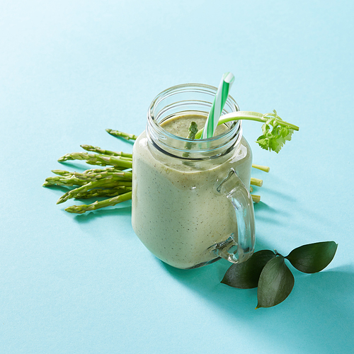 Vegetarian healthy smoothies from green vegetables with green leaves and plastic straw in a glass bowl on green paper background.