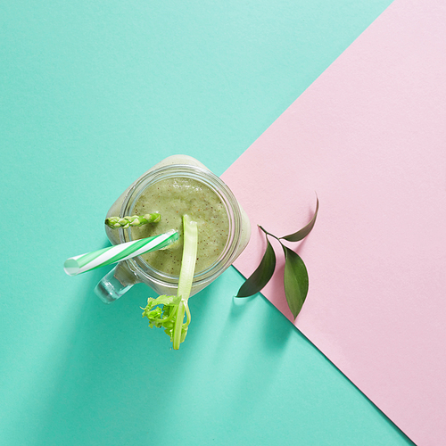 Vegetarian healthy smoothies from green vegetables with green leaves and plastic straw in a glass bowl on duotone pink green paper background. Top view.