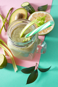 Vegetarian healthy smoothies from green vegetables with green leaves, slices of lemon, avocado, cocumber and plastic straw in a glass bowl on duotone pink green paper background.