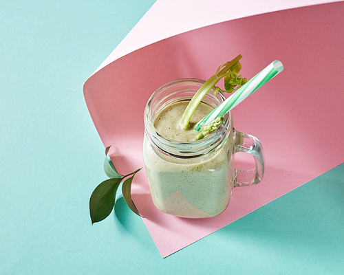 Vegetarian healthy smoothies from green vegetables with green leaves and plastic straw in a glass bowl on duotone pink green paper background. Pink paper twisted in any shape.