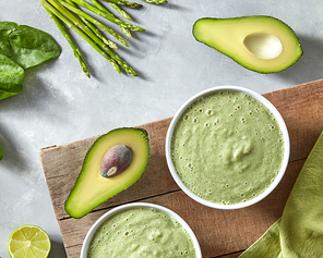 Homemade green healthy smoothies from spinach, avocado and asparagus in a bowl on a wooden board with a green napkin on a concrete background