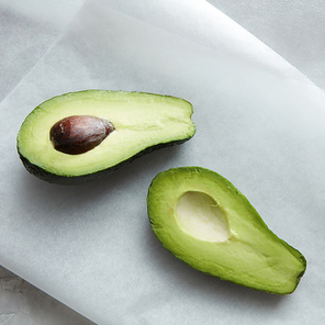 Fruit avocado represented on white baking paper over table. Green colored avocado with brown bone.