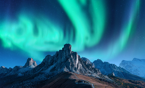Aurora borealis above mountains at night in Europe. Northern lights. Sky with stars with polar lights and high rocks. Beautiful landscape with aurora, buildings on the hill, mountain ridge. Travel