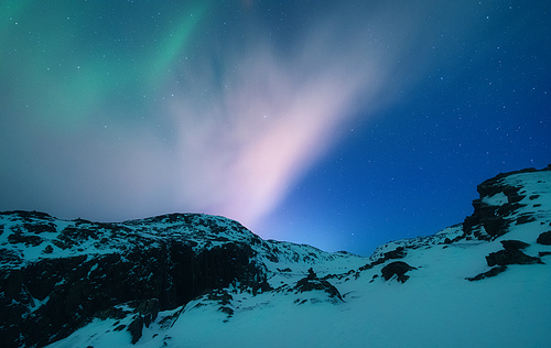 Aurora borealis above the snow covered mountain range in europe. Northern lights in winter. Night landscape with green polar lights and snowy mountains. Starry sky with aurora. Nature. Space