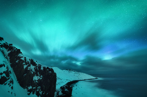 Amazing aurora borealis. Northern lights in Teriberka, Russia. Starry sky with polar lights and clouds. Night winter landscape with aurora, sea with stones in blurred water, snowy mountains. Travel