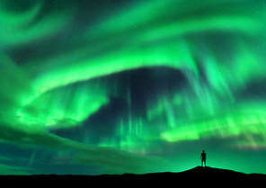 Aurora borealis and silhouette of standing man. Lofoten islands, Norway. Aurora and happy man. Sky with stars and green polar lights. Night landscape with aurora and people. Concept. Travel background