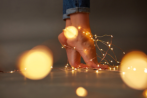 Christmas garlands on the floor are decorated with female feet around a dark background with a blur of yellow lights. Copy space