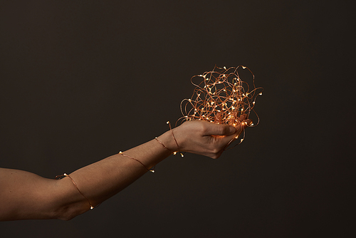 A woman's hand wrapped in a Christmas garland holds a fire in her hand on a dark background