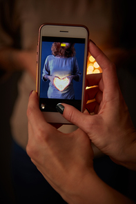 The phone with the image of a girl with a glowing heart is holding a woman in a blurred background with a beautiful bokeh.