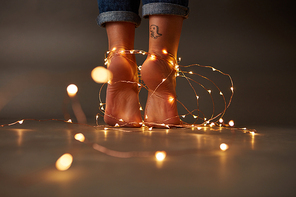 Tattoo feet of the woman decorated with a festive Christmas garland on a dark background. Holiday concept