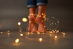Beautiful female feet with yellow Christmas garlands on the floor around a dark background with space for text. Celebration
