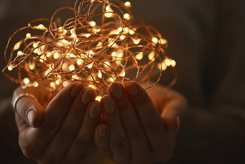 bright christmas lights garland in the hands of a woman on a dark background