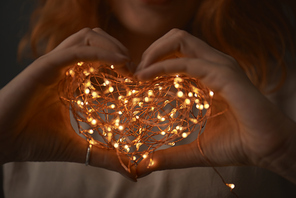 Female hands holding a Christmas string of lights in the form of a heart on a dark background
