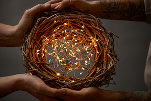 two girls holding a beautiful wreath of twigs with bright Christmas lights in hands on a dark background flat lay