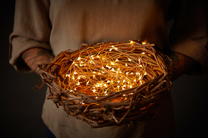 woman tattoo hands holding a nest decoration with lights on dark background. spring and . holiday concept