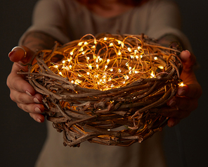 Woman hands holding a nest with lights on dark background. Easter holidays inspiration