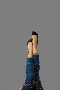 A girls legs tied with a Christmas garland in shoes and jeans on a gray background with copy space.