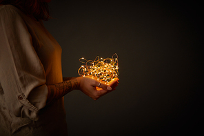 in the hands of a woman a Christmas garland of lights on a dark background
