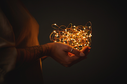 yellow christmas lights garland in a female hand on a dark background