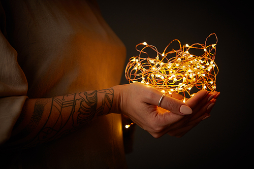 Female tattoo hands holding yellow Christmas light decorations on dark holiday background. Xmas and New Year theme