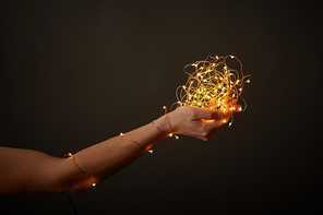 A girl's hand holds a bunch of bright garlands around a dark background with copy space. Christmas celebration