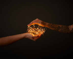 Bright yellow garland holds female hand with tattoo and male hand around a dark background with space for text.