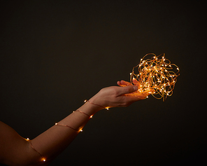 A woman's hand holds bright Christmas lights on a black background with space for text. Creative holiday layout