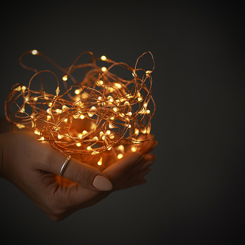garland of christmas lights in a female hand on a dark background