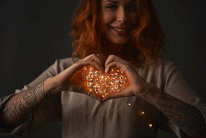girl holds hands in the form of heart with Christmas lights